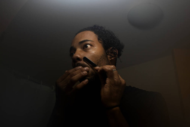 Afro latin guy shaving by himself with a razor blade. - Foto, imagen
