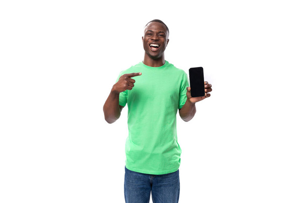 ένας νεαρός 30χρονος Αμερικάνος ντυμένος άνετα με ένα βασικό μπλουζάκι και τζιν διαφημίζει ένα smartphone. - Φωτογραφία, εικόνα