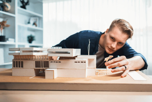 Arquitecto diseñador estudia elegante modelo de casa, revisando el diseño de la estructura para la mejora con el plan de construcción en la mesa. Creatividad e innovación en el diseño arquitectónico. Iteración - Foto, Imagen