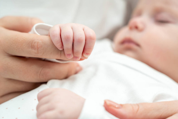 Il primo piano rivela un neonato che tiene per mano le madri, simbolo di sicurezza e affetto materno - Foto, immagini