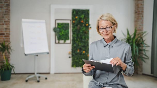 Portrait of one mature blonde caucasian woman with eyeglasses in the office at work happy smile looking to the camera confident copy space - Fotoğraf, Görsel