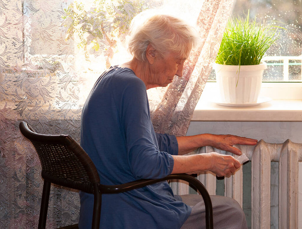 La donna anziana che tiene la bolletta del gas davanti al termosifone. Pagamento per riscaldamento in inverno. - Foto, immagini