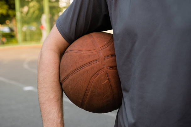 Basketball ball in the hand of a man on the outdoor sports ground. - Фото, зображення