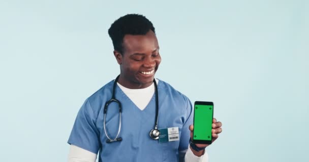 Медсестра, щасливий чоловік, який показує телефон і зелений екран в студії для телевізійного здоров'я, онлайнової охорони здоров'я та експертної поради. Медичний працівник, доглядач або лікар з цифровим додатком для здоров'я на синьому фоні. - Кадри, відео