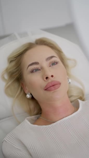 Une femme se regarde dans le miroir après l'augmentation des lèvres et le lifting dans un salon de beauté - Séquence, vidéo
