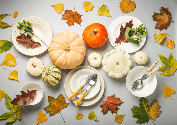 Composición de mesa festiva de Acción de Gracias con diferentes calabazas de colores, hojas de otoño, platos vacíos con cubiertos en la mesa de fondo gris claro listo para la fiesta y la celebración.. - Foto, imagen