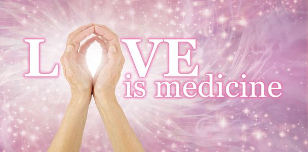 Liebe ist Medizin und der ultimative Heiler - Frauenhände, die das O der LIEBE IST MEDIZIN auf einem strahlend fließenden Hintergrund herstellen  - Foto, Bild
