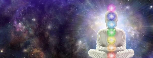 Meditating Chakra Buddha sitting in lotus position surrounded by  deep space - buddha on right side with seven chakras against a starry dark blue celestial sky with a massive nebula and copy space for text  - Photo, Image