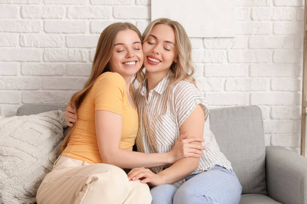Young sisters hugging on sofa at home - Foto, afbeelding
