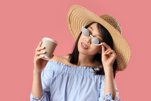 Krásná asijská žena ve stylové sluneční brýle s šálkem kávy na růžovém pozadí - Fotografie, Obrázek