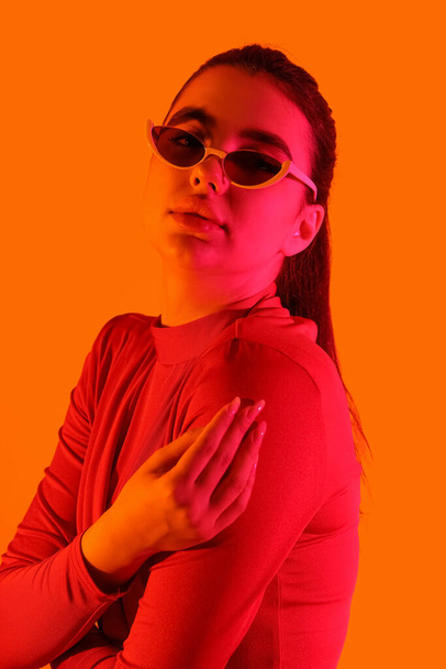 Модна молода жінка в сонцезахисних окулярах на помаранчевому фоні - Фото, зображення