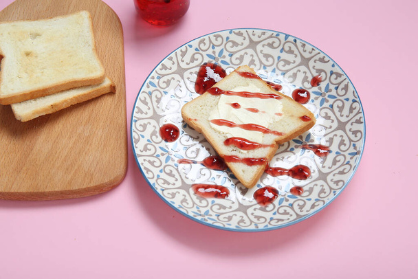 Plate of toast with butter and jam on pink background - Photo, Image