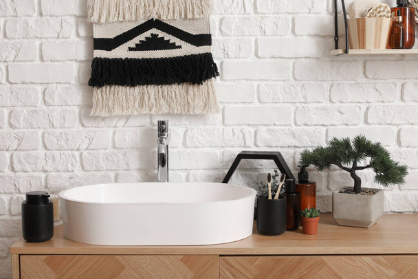 Sink bowl, cup with toothbrushes, houseplant and bonsai tree on wooden cabinet in bathroom - Photo, Image
