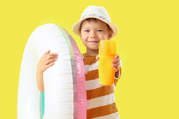 Kleiner Junge mit einer Flasche Sonnencreme und einem aufblasbaren Ring auf gelbem Hintergrund - Foto, Bild