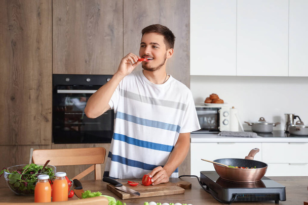 キッチンでカットトマトを食べる若い男 - 写真・画像