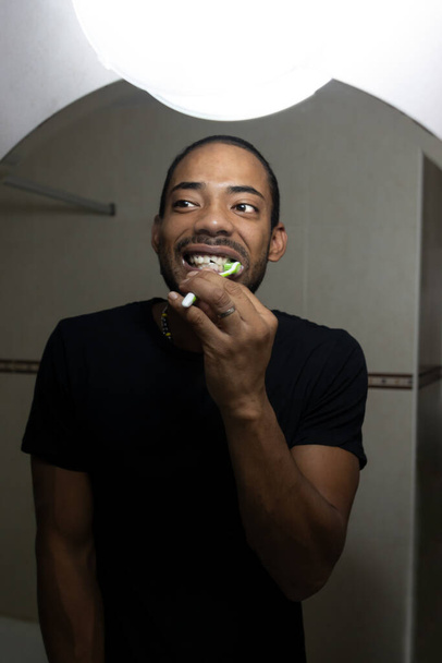 Colombian man brushing his teeth while looking in the mirror - Φωτογραφία, εικόνα