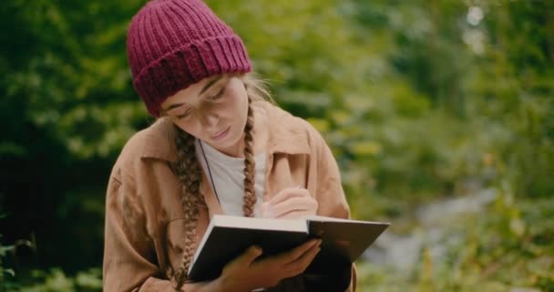 Jeune touriste féminine avec des cheveux tressés écrit en livre pendant les vacances - Séquence, vidéo