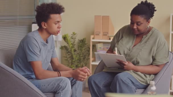 Medium traagheid van boos Biraciale tiener jongen met gesprek met zwarte vrouwelijke psycholoog in het kantoor - Video