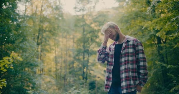 Szomorú fiatal férfi turista, fejjel a kézben áll a fák mellett az erdőben - Felvétel, videó