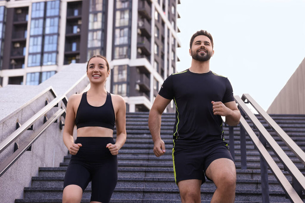 Healthy lifestyle. Happy couple running on steps outdoors, low angle view - Foto, imagen