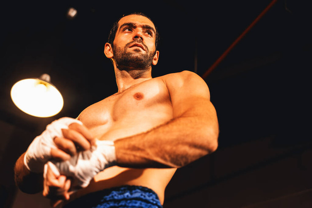 Biały portret boksera z muskularnym i wysportowanym ciałem owijającym dłoń lub pięść na ringu być przed bokserskim pojedynkiem lub treningiem. Impetus - Zdjęcie, obraz