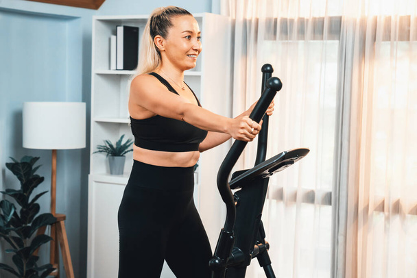 Actieve senior vrouw draait op elliptische loopmachine thuis portret als fitness gezonde levensstijl en lichaamsverzorging na pensionering voor gepensioneerde. Klok - Foto, afbeelding