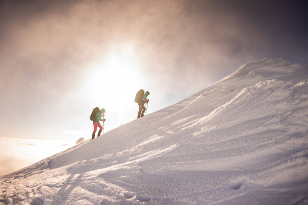 Két lány hátizsákkal és hótalppal sétál a hóban hóviharban. hegymászás a nagy hegyekben. - Fotó, kép