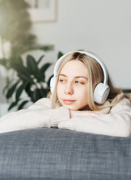 Jeune femme blonde dans un casque écoutant de la musique et se relaxant à la maison. - Photo, image