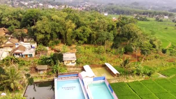Piscina privada desde un resort, con un telón de fondo de vistas de campos de arroz en un día soleado. Vista aérea desde el dron de una piscina privada en el borde de los campos de arroz, a las afueras de Bandung, Indonesia. Alta calidad 4K Drone metraje - Metraje, vídeo