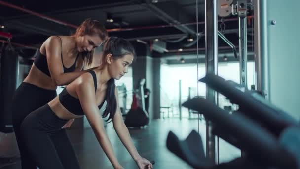 Young Asian woman doing exercises in fitness gym, exercises to strengthen muscles and strength with personal trainer. Fitness exercising in gym. - Footage, Video