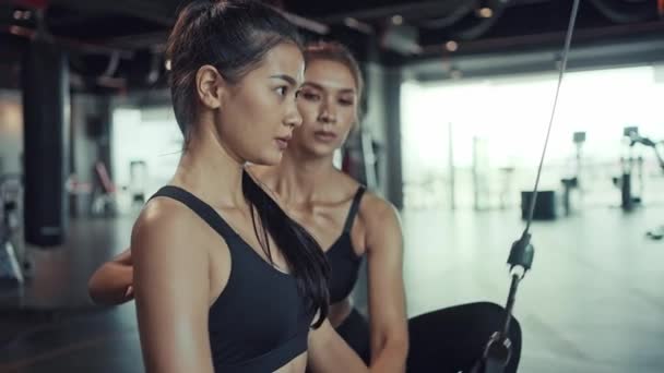Mujer asiática joven haciendo ejercicios en el gimnasio de fitness, ejercicios para fortalecer los músculos y la fuerza con entrenador personal. Ejercicio de fitness en gimnasio. - Imágenes, Vídeo