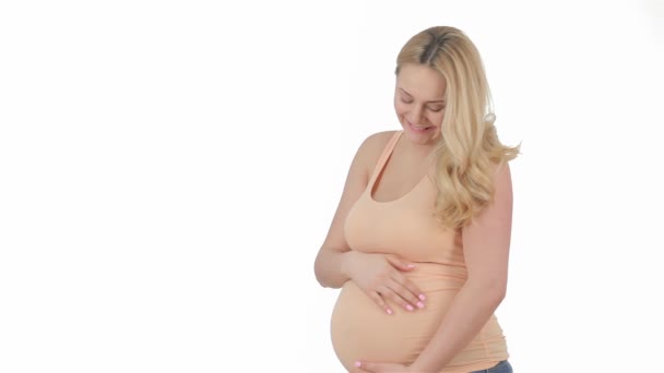 Terhes szőke finoman simogatni a hasát a stúdióban. Elég terhes nő örvendeznek a terhesség. Mosolygó terhes nő izolált fehér háttér - Felvétel, videó