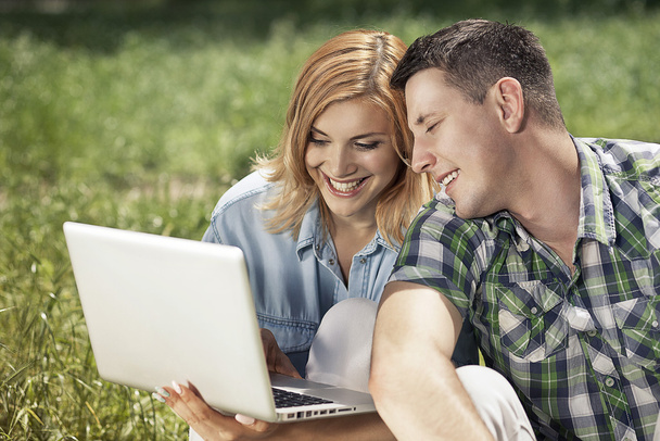 Wesoły młoda para siedzi na trawie, patrząc na laptopa - Zdjęcie, obraz
