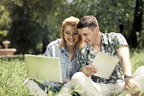 Young attractive couple sitting on the grass, looking at laptop  - Fotoğraf, Görsel