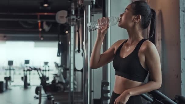 Jonge Aziatische vrouw drinken water uit fles tijdens de training in de sportschool. Fitness atleet mooi meisje dragen sportswear met vermoeide fit houd water fles in de hand. - Video