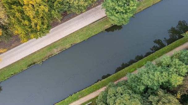 Dit betoverende luchtperspectief biedt een top-down uitzicht op een vredig kanaal dat zich een weg baant door een weelderig, groen landschap. Towering bomen langs de waterkant, het creëren van een schilderachtige scène van - Foto, afbeelding