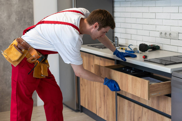 Reparador em macacões Reparação gabinete dobradiça na cozinha
. - Foto, Imagem
