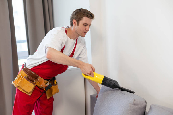 Rückansicht junger männlicher Arbeiter putzt Sofa mit Staubsauger. - Foto, Bild