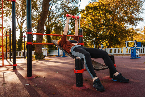 Femme blanche mi-adulte fait banc français presse se trouve sur le banc de formation dans le parc de la ville. Concept de fitness et de sport. - Photo, image