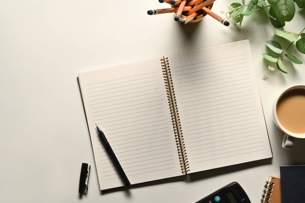 Carnet vierge avec stylo, tasse à café et porte-crayon sur bureau blanc. Vue du dessus avec espace pour le texte. - Photo, image