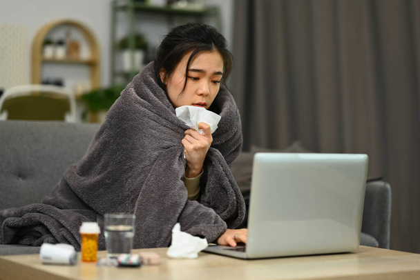 Mujer joven envuelta en manta que tiene consulta médica en línea en el ordenador portátil. Concepto de salud y tecnología. - Foto, imagen