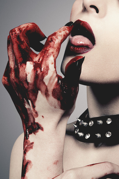 Sexy young woman licks blood against grey background - Фото, зображення