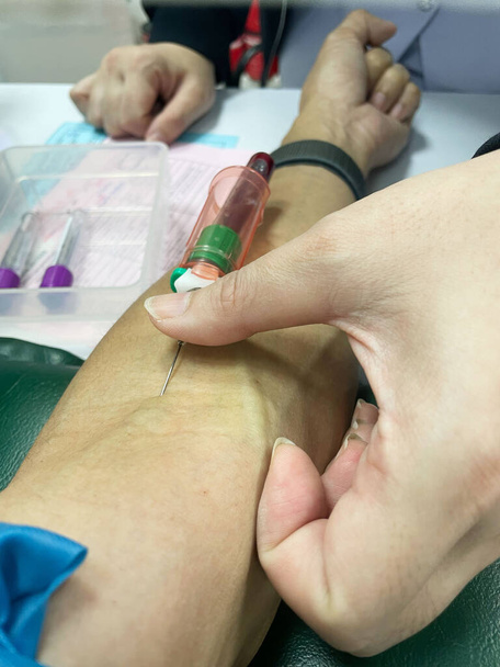 Μια νοσοκόμα τρυπώντας φλέβα του ασθενούς και αντλώντας δείγμα αίματος σε σωλήνα δείγματος για εξέταση. - Φωτογραφία, εικόνα