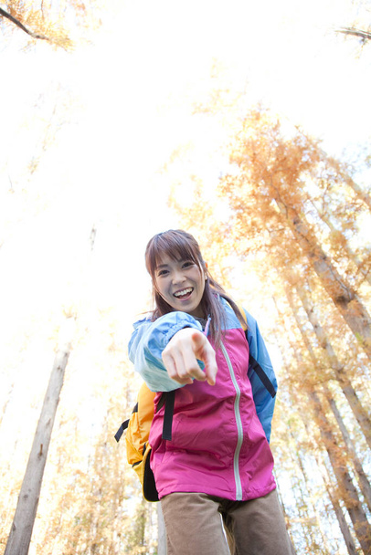 Young Japanese woman with yellow backpack trekking in autumnal park - Fotoğraf, Görsel