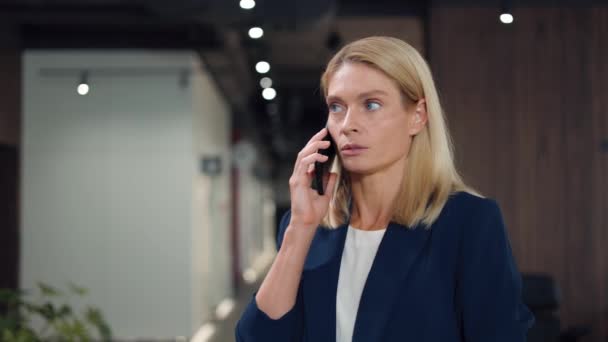 Attractive caucasian woman talking seriously on modern smartphone with business colleague. Blonde female wearing stylish business suit calmly explaining opinion to interlocutor in office center. - Footage, Video