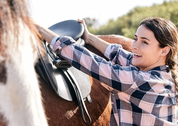 Horse, happy rider and woman with saddle on ranch for animal care, training and riding on farm. Agriculture, countryside and person with seat for stallion for practice, freedom and adventure outdoors. - Photo, Image