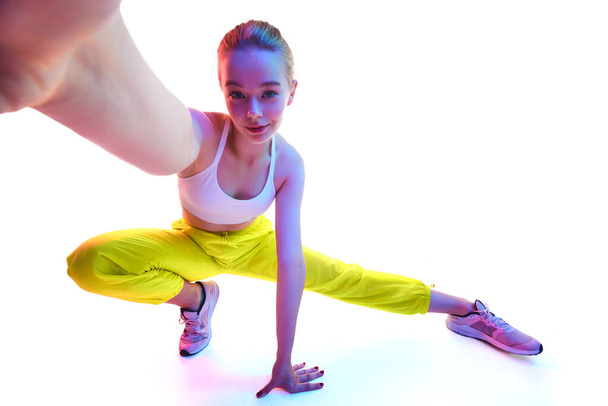 From below portrait of attractive young woman training in trendy sport outfit in neon light while reaching out hands towards camera. Concept of sport, fashion, active lifestyle, youth, ad. Copy space - Photo, Image