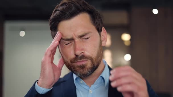 Front view of stressed brunette man having terrible headache after intense working day in office. Bearded male person dressed in formal wear closing eyes and massaging temples to relief strong pain. - Footage, Video