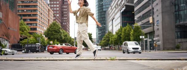 Портрет азиатской счастливой девушки, прыгающей и танцующей в центре города, позирующей на улицах, выражающей радость и волнение. Копирование пространства - Фото, изображение