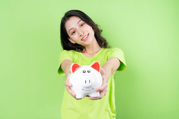 アジアの少女は彼女の手でお金を節約するコンセプトに豚バンクを持っています - 写真・画像